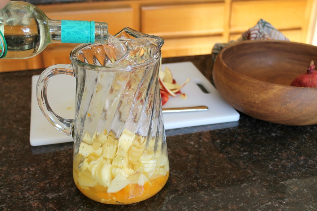 How to make a basic white wine sangria via SpanglishSpoon.com A bottle of Moscato wine being poured into a large glass pitcher.
