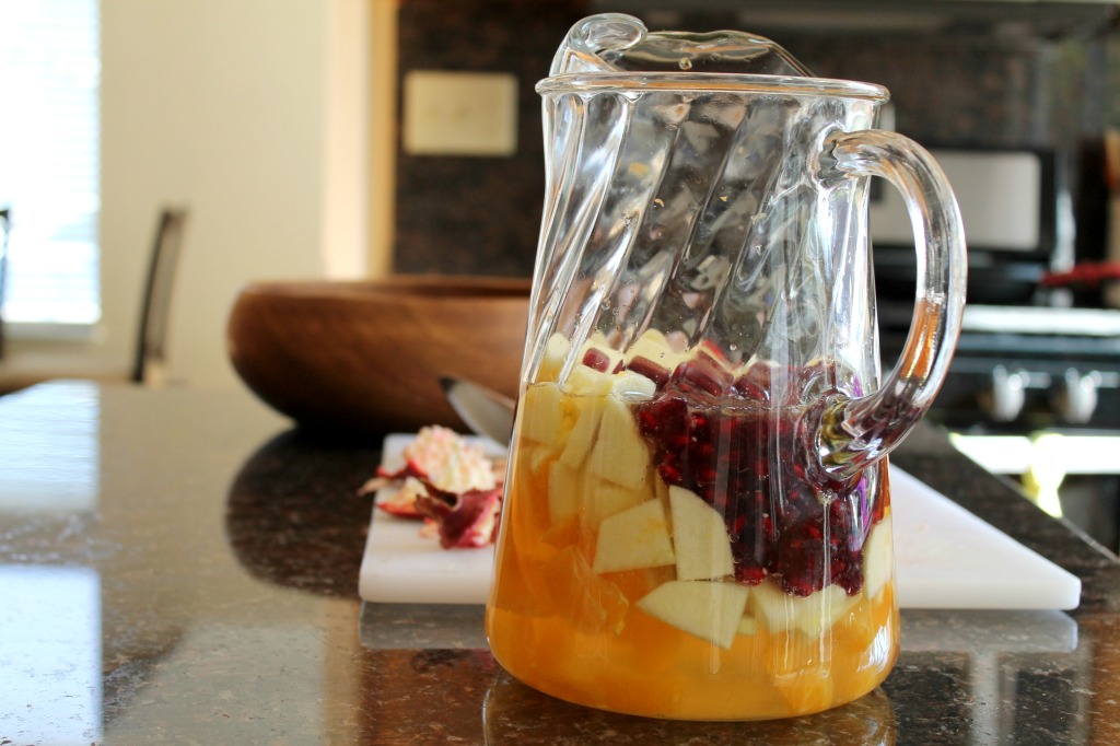 A large glass pitcher with Moscato wine, peeled and sliced fruit and pomegranate arils.