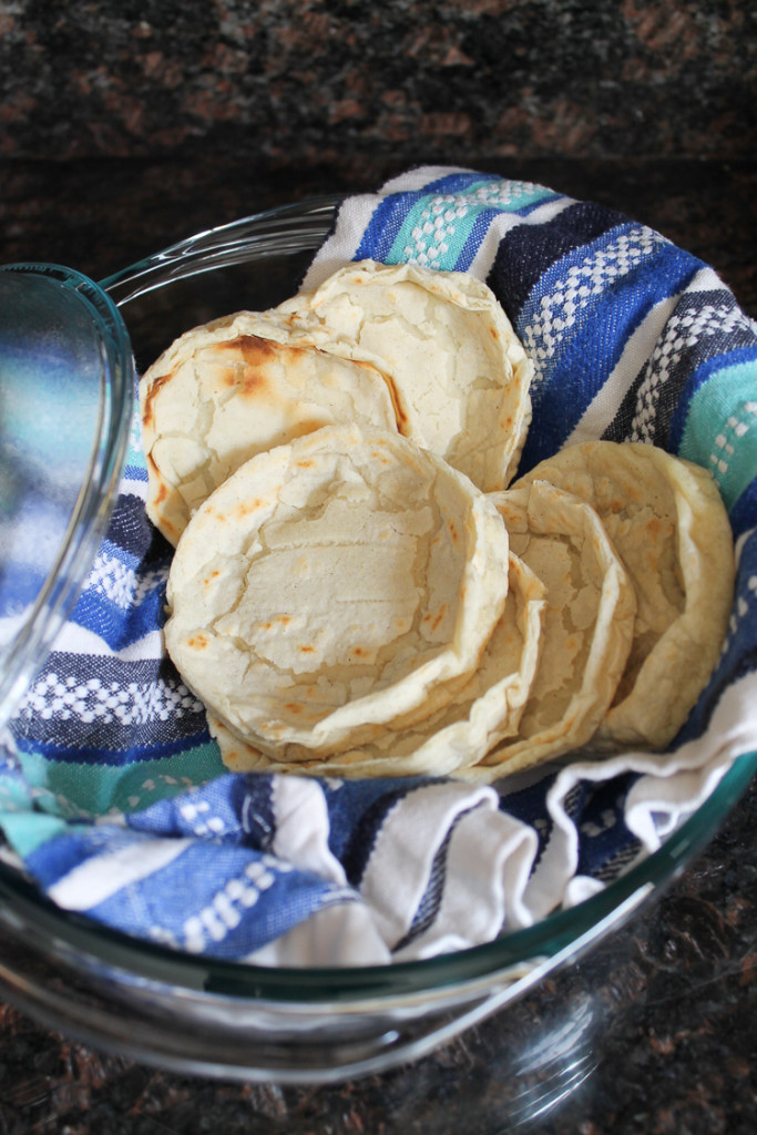 Fresh made sope shells cooling on a dish towel in a shallow baking dish.