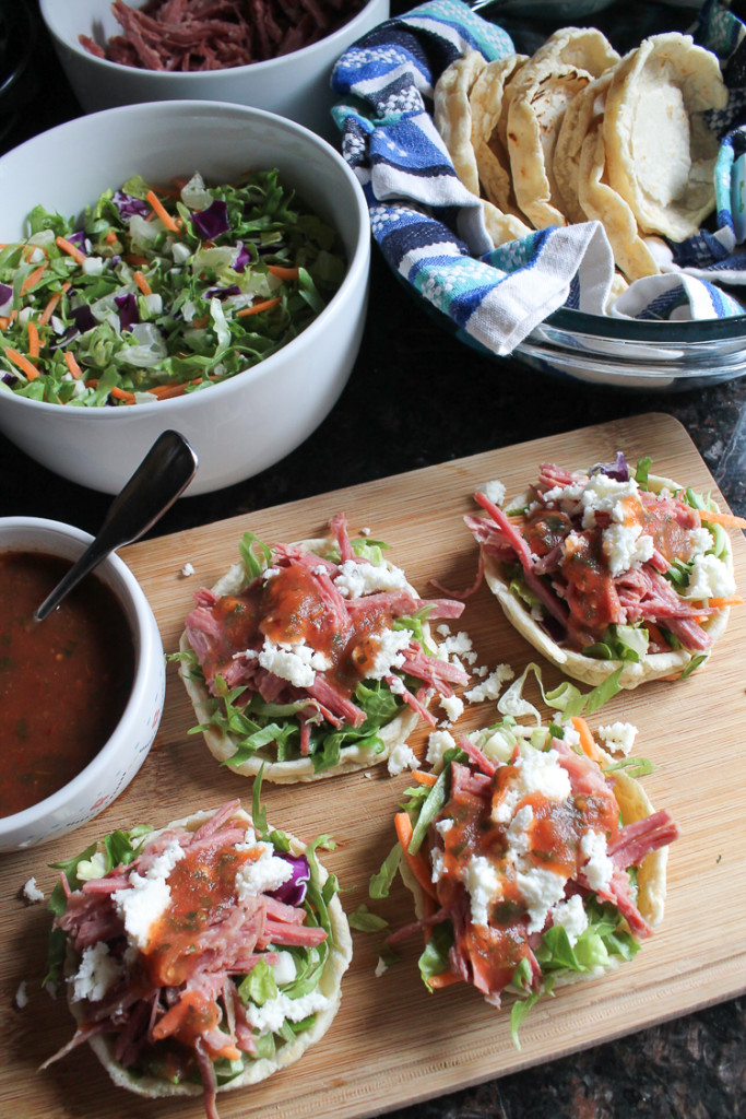 Homemade sopes shells with chopped lettuce, slow-cooked shredded corned beef, queso fresco and red salsa.