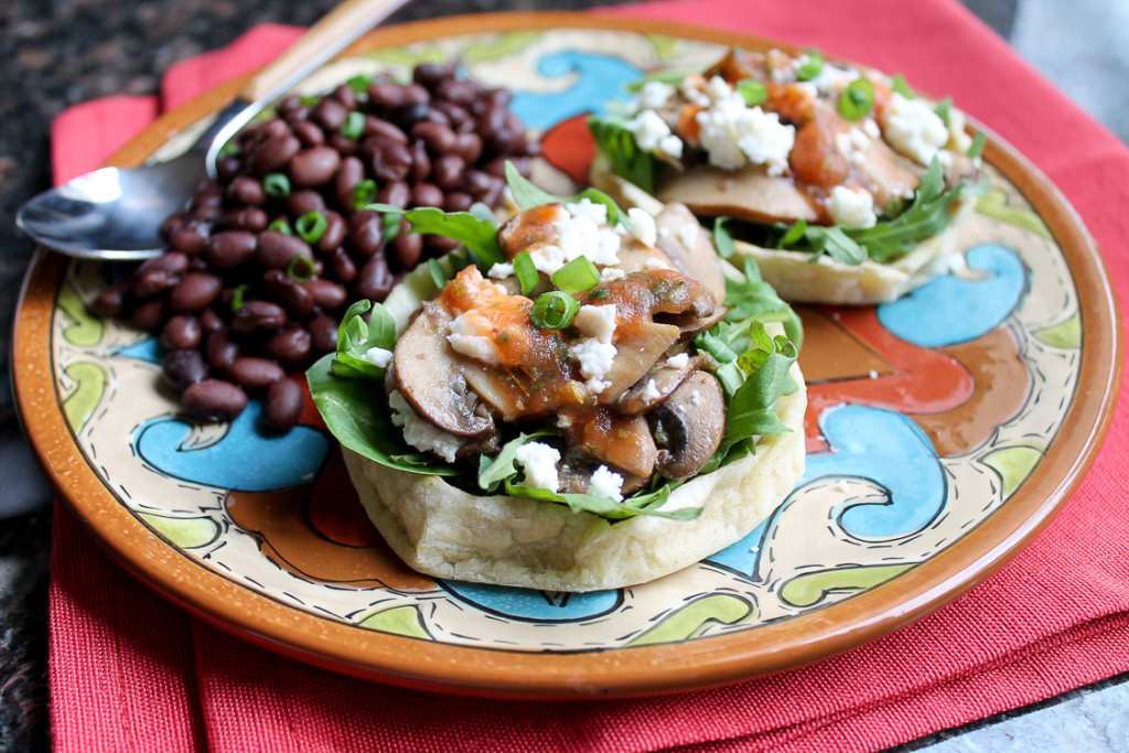Homemade Sopes topped with baby arugula, spinach, requeson cheese, and red salsa.
