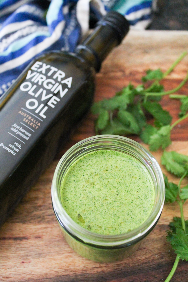 Dairy-Free Low-Fat Cilantro Dressing via SpanglishSpoon.com Bottle of Extra Virgin Olive Oil next to a glass jar filled with a homemade cilantro dressing.