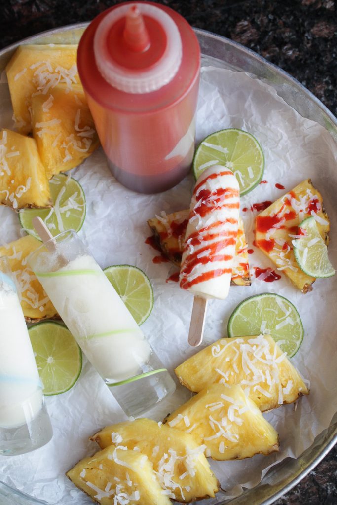 Pineapple and lime slices with shot glass size coconut pineapple and lime popsicles, drizzled with chamoy sauce.