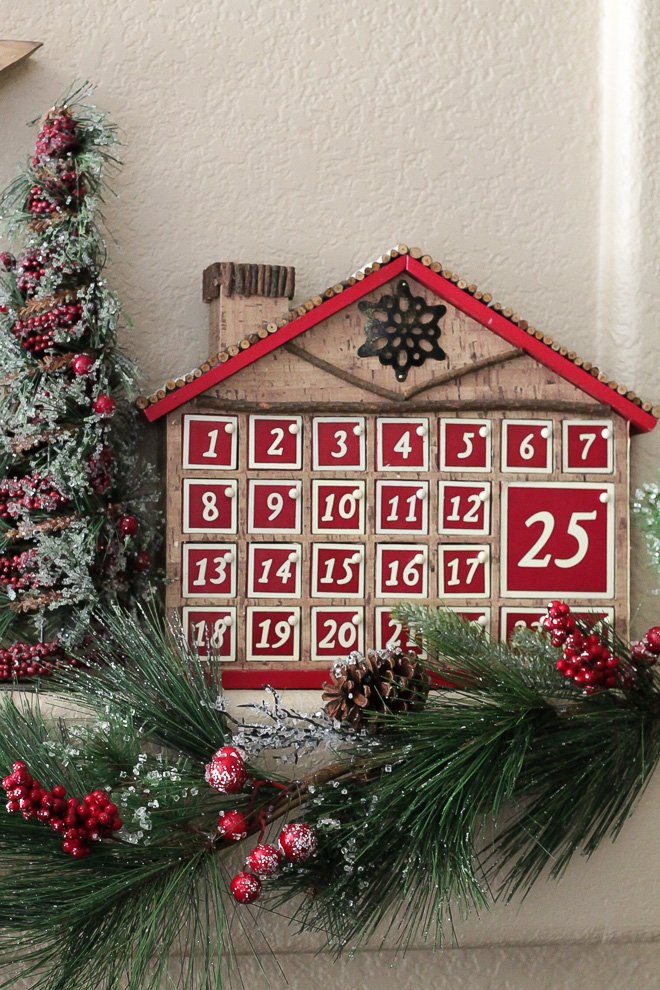 Advent calendar house with 25 doors placed on a mantel with Chrismas decor.