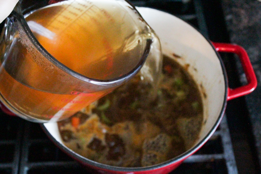 Vegetable broth being poured into a pot of soup.