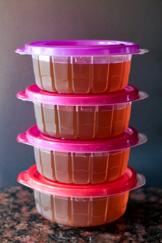 Four plastic containers filled with vegetable broth, stacked on top of each other.