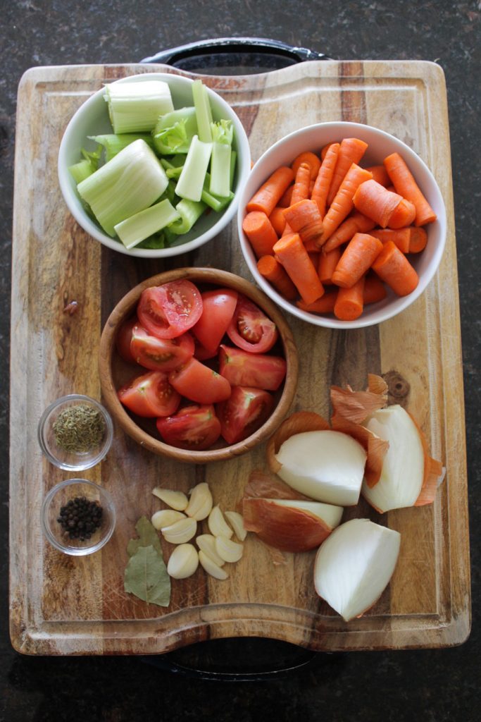 Carrot, celery, tomatoes, yellow onion, garlic, spices prepped for a vegetable broth recipe.