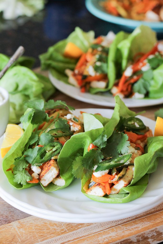 Sautéed tofu and vegetables wrapped in butter lettuce leaves, topped with sliced serrano chiles and cilantro sprigs.