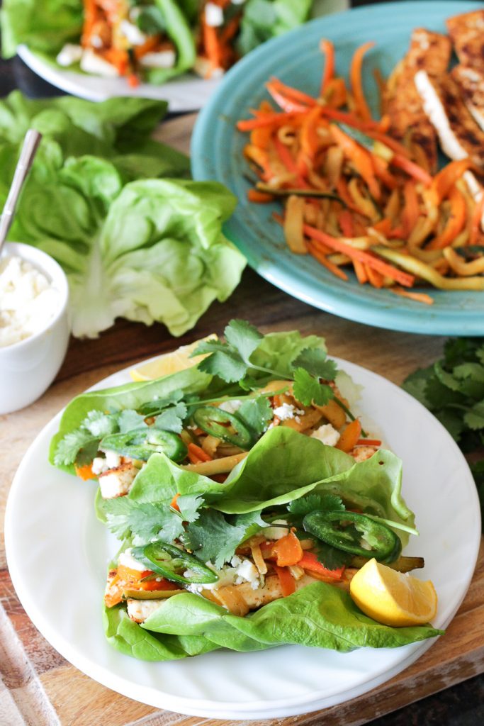Sautéed tofu and vegetables wrapped in butter lettuce leaves, topped with sliced serrano chiles and cilantro sprigs.