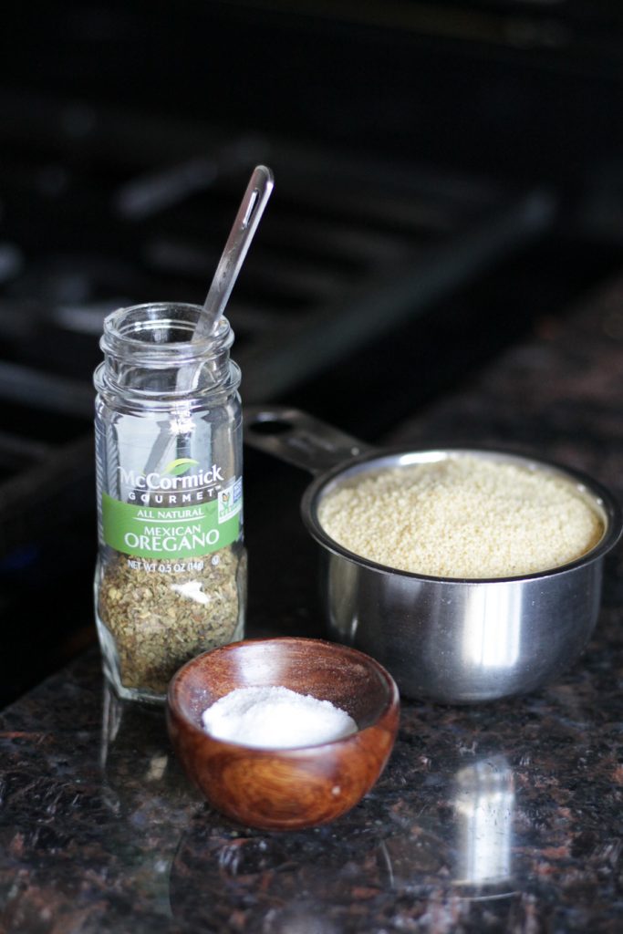 McCormick bottle of Mexican oregano, couscous in a measuring cup, small wooden bowl with salt.