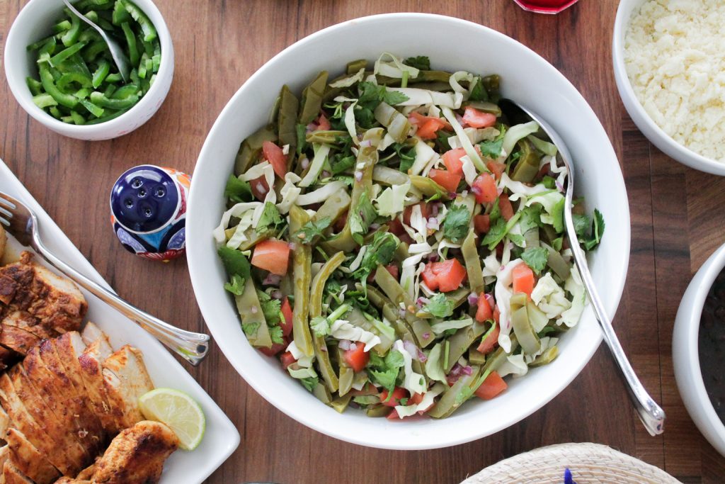 cooked cactus salad with cabbage and tomatoes in a white serving bowl on a dinner table.